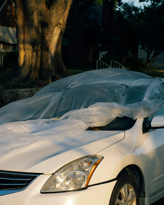 a white car covered in plastic sitting on the side of the road