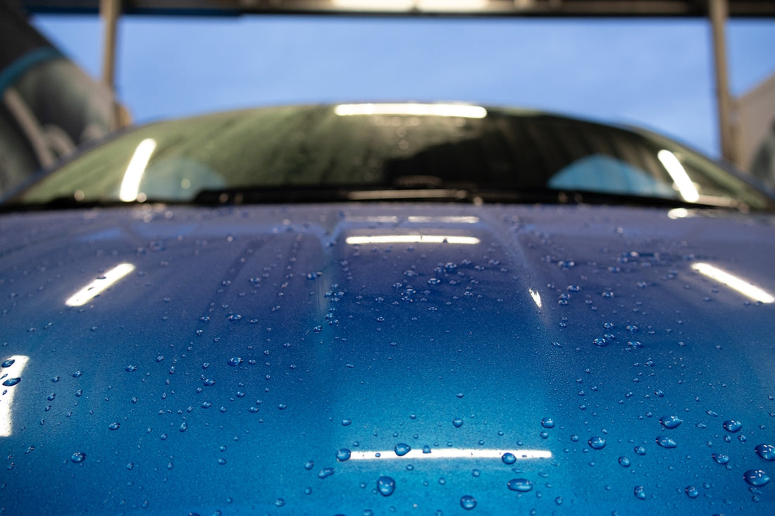 the hood of a blue car with water droplets on it