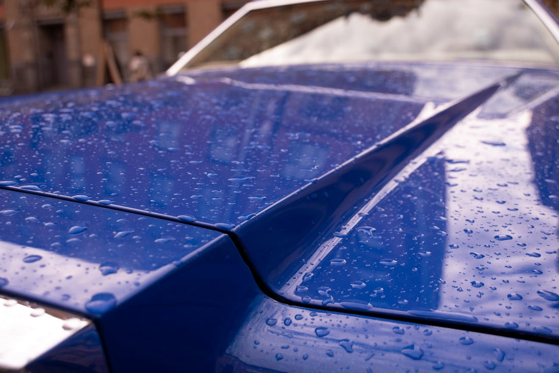 Raindrops dapple a glossy blue car hood.
