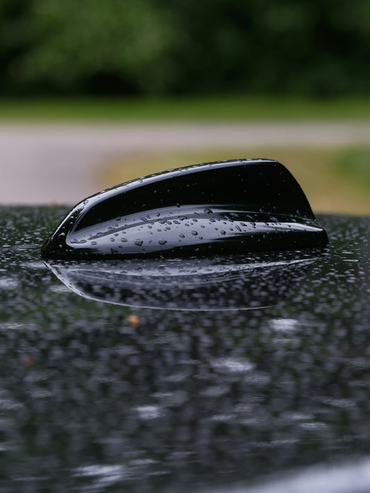 Raindrops adorn a car's black antenna.